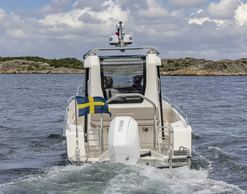 A motorboat with a Swedish flag navigates through calm waters, showcasing its sleek design and engine at the rear.